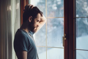 An introvert stands in front of a window, looking sad.