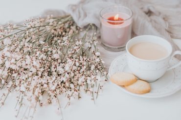 a candle, cookies, coffee, and flowers, representing an introvert's hygge all year round